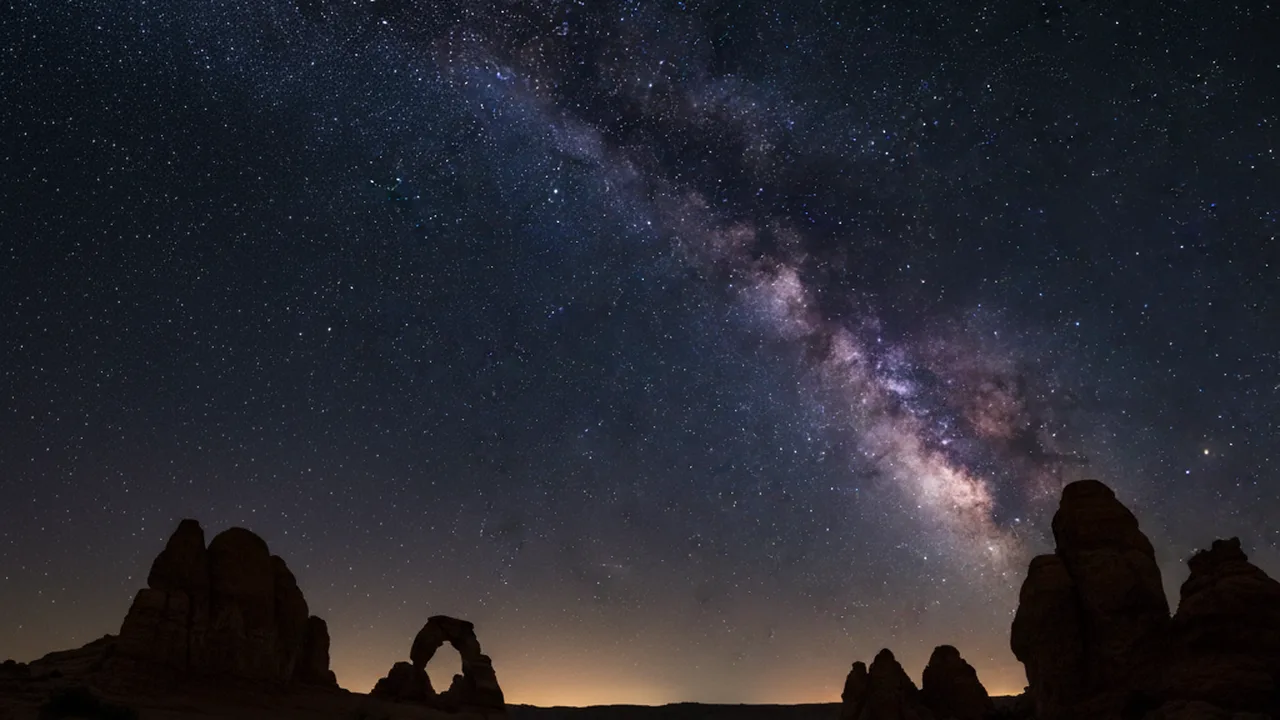 Milky Way galaxy stretching across dark night sky over desert landscape